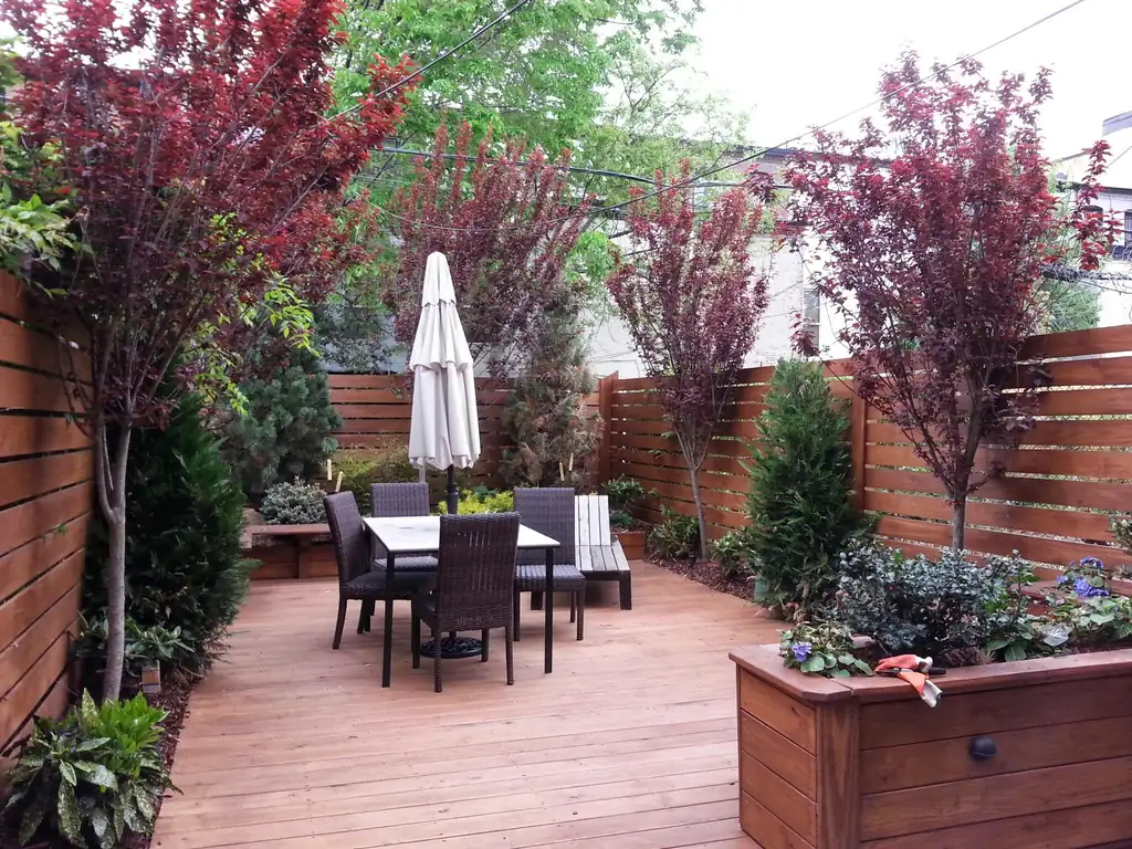 Courtyard patio with a dining set, umbrella and raised planters and red-leaf trees