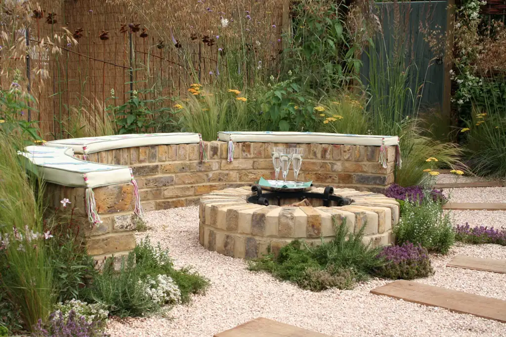 Round stone fire pit surrounded by a curved seat wall and plantings