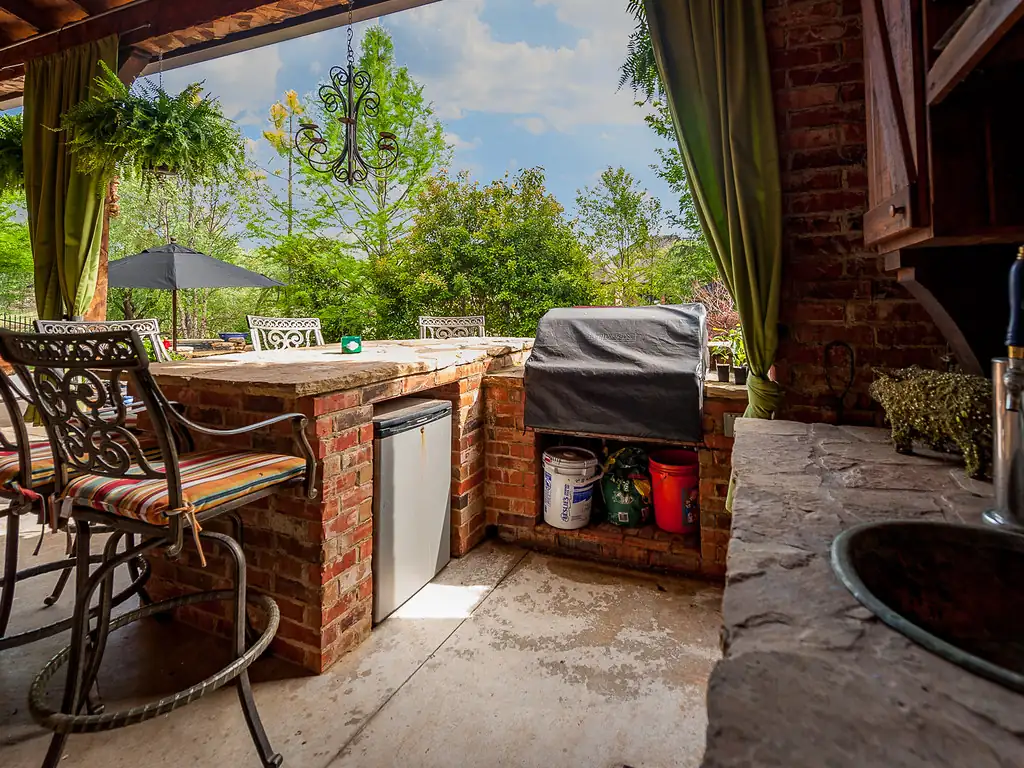 Covered outdoor kitchen with a built-in grill, stone counters and bar seating